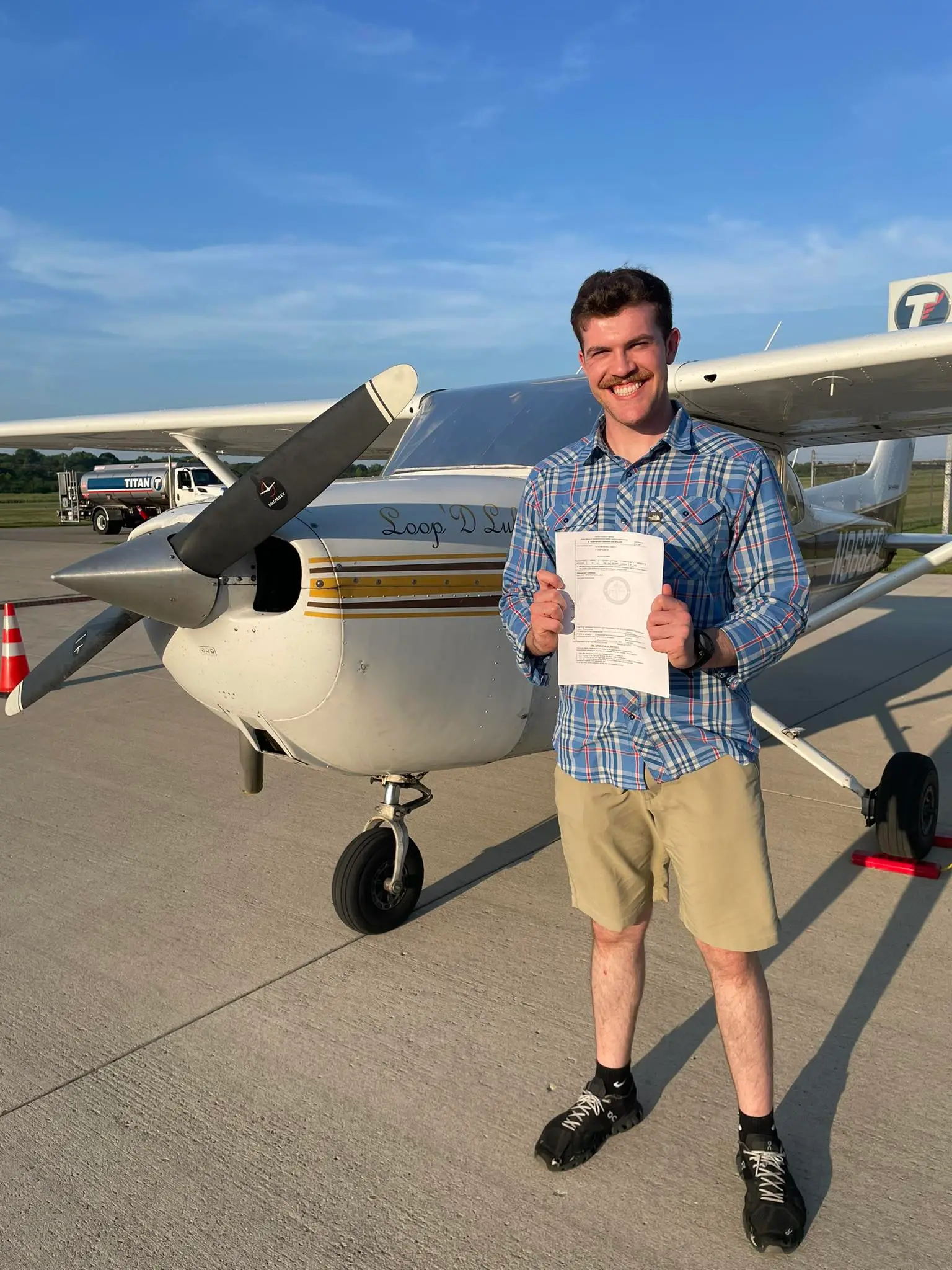 Student holding certificate standing in front of a plane at Dayton Aviation Services